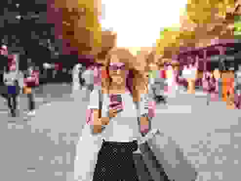 A women standing with shopping bags smiling at her phone